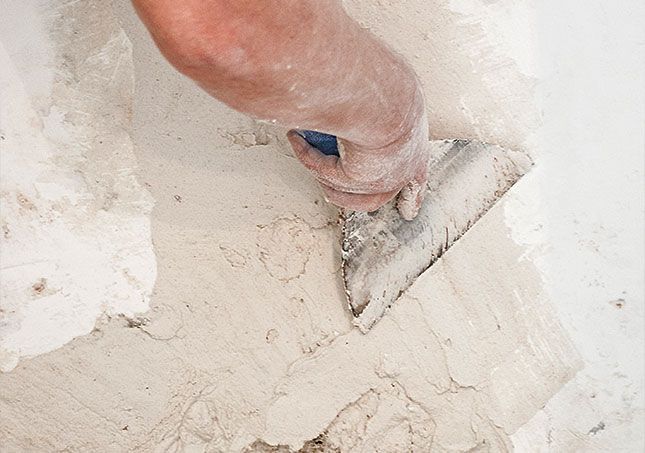 Hand using a trowel to smooth wet plaster on a white wall surface
