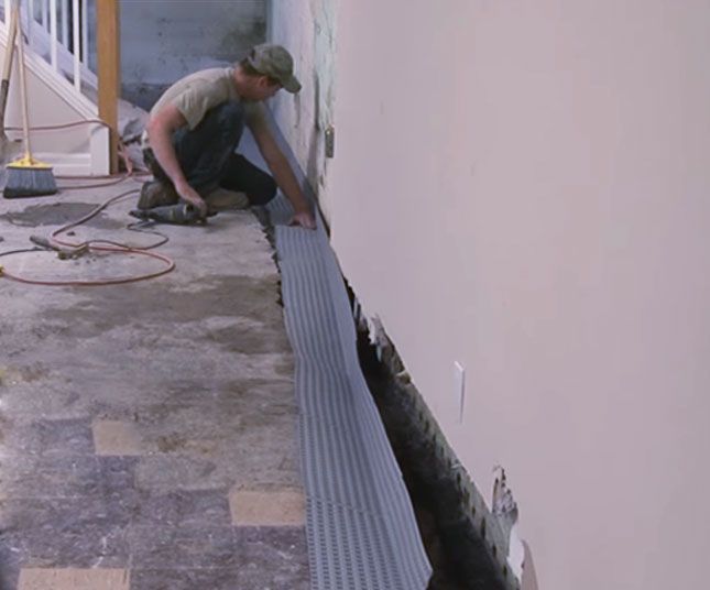 Worker installing a long metal drainage grate along a building wall
