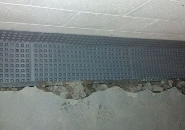 Damaged wall beneath a textured blue-gray ceiling panel with exposed rubble and concrete