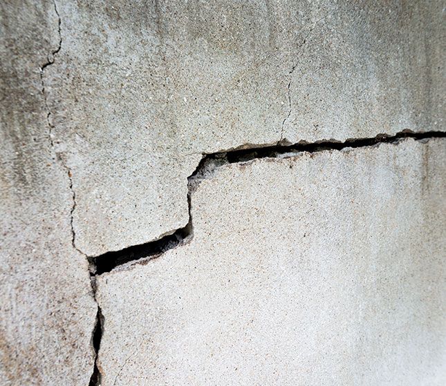 Close-up of a cracked, weathered concrete wall with a jagged horizontal fissure