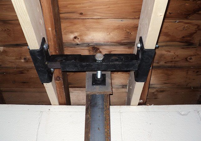 Black metal bracket attached to a wooden ceiling beam and vertical support post.