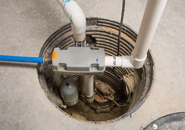 Open underground utility pit with pipes, valves, and a gray control box connected to blue and white lines.