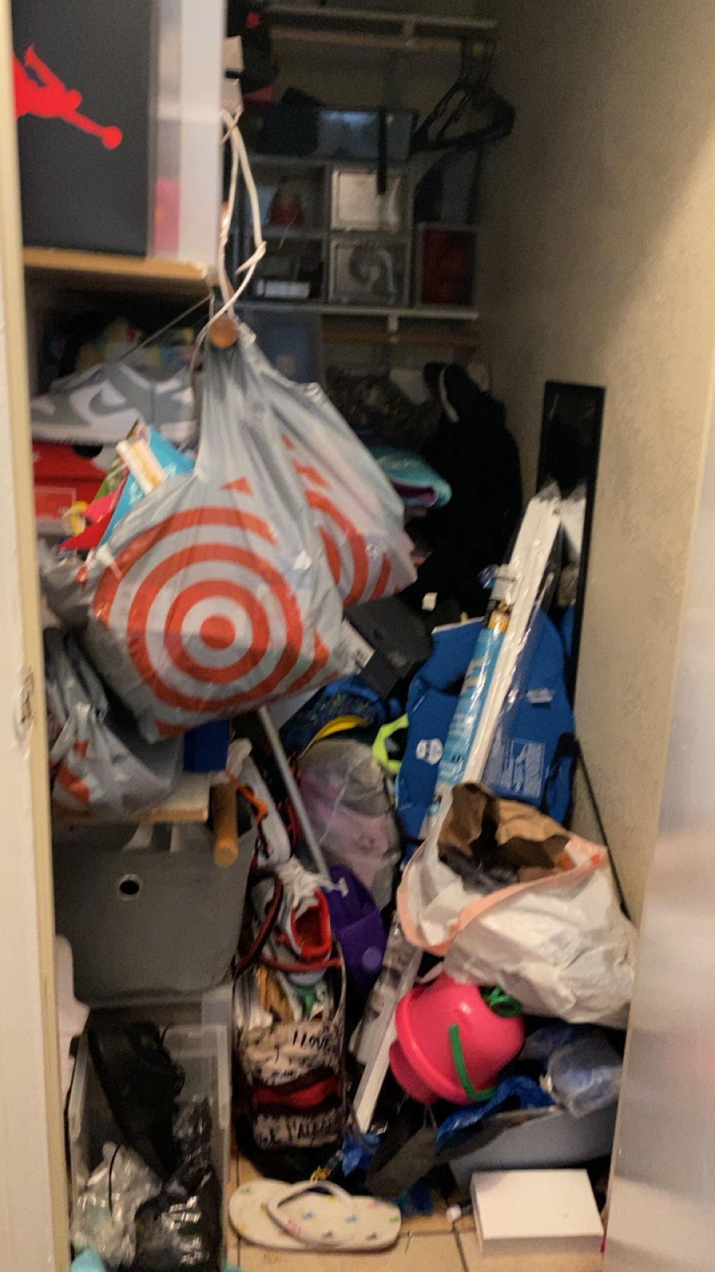 Cluttered narrow closet packed with bags, boxes, and household items, including a red-and-white Target bag.