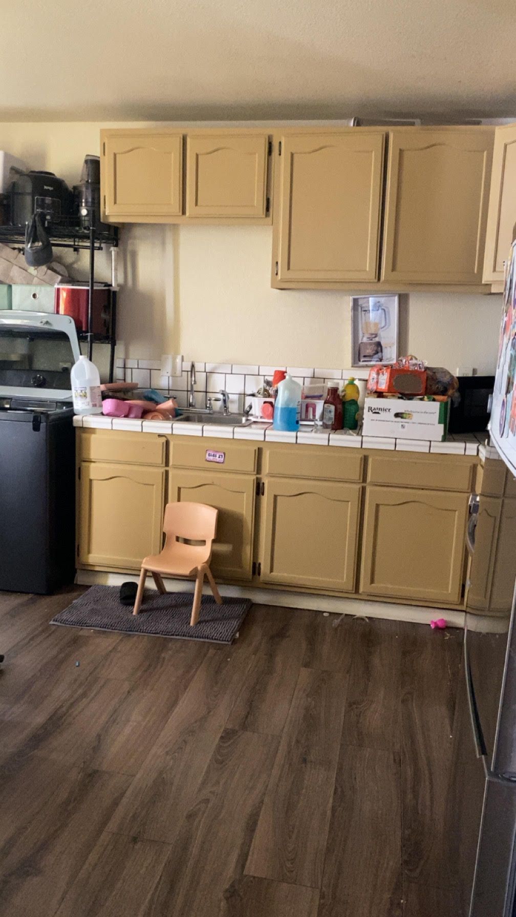 Small kitchen with beige cabinets, wood-look floor, and a childβs chair in front of the counter.