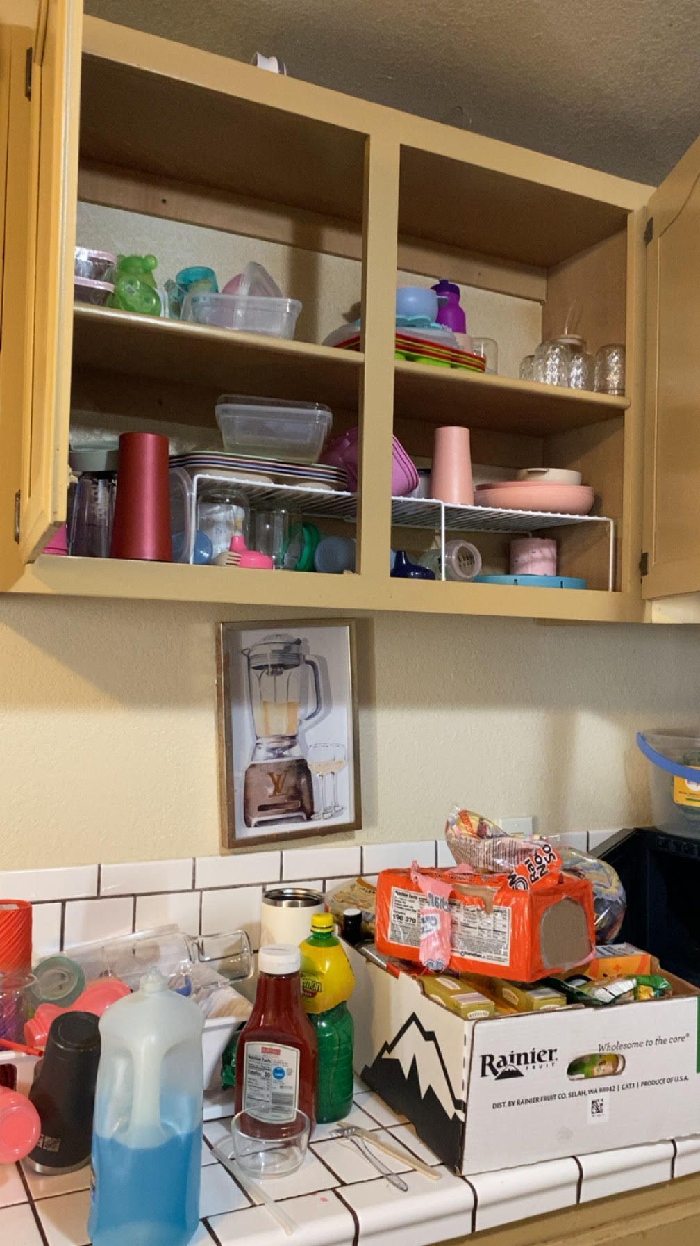 Kitchen cabinets open over a cluttered countertop with household items and cleaning supplies