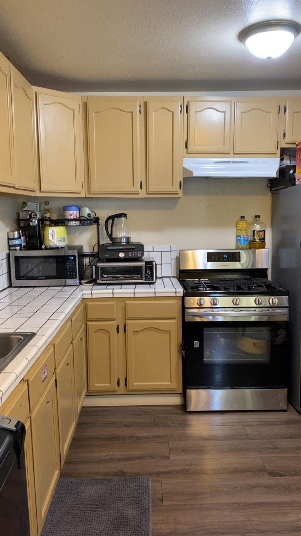 Small kitchen with beige cabinets, black appliances, and wood-look flooring.