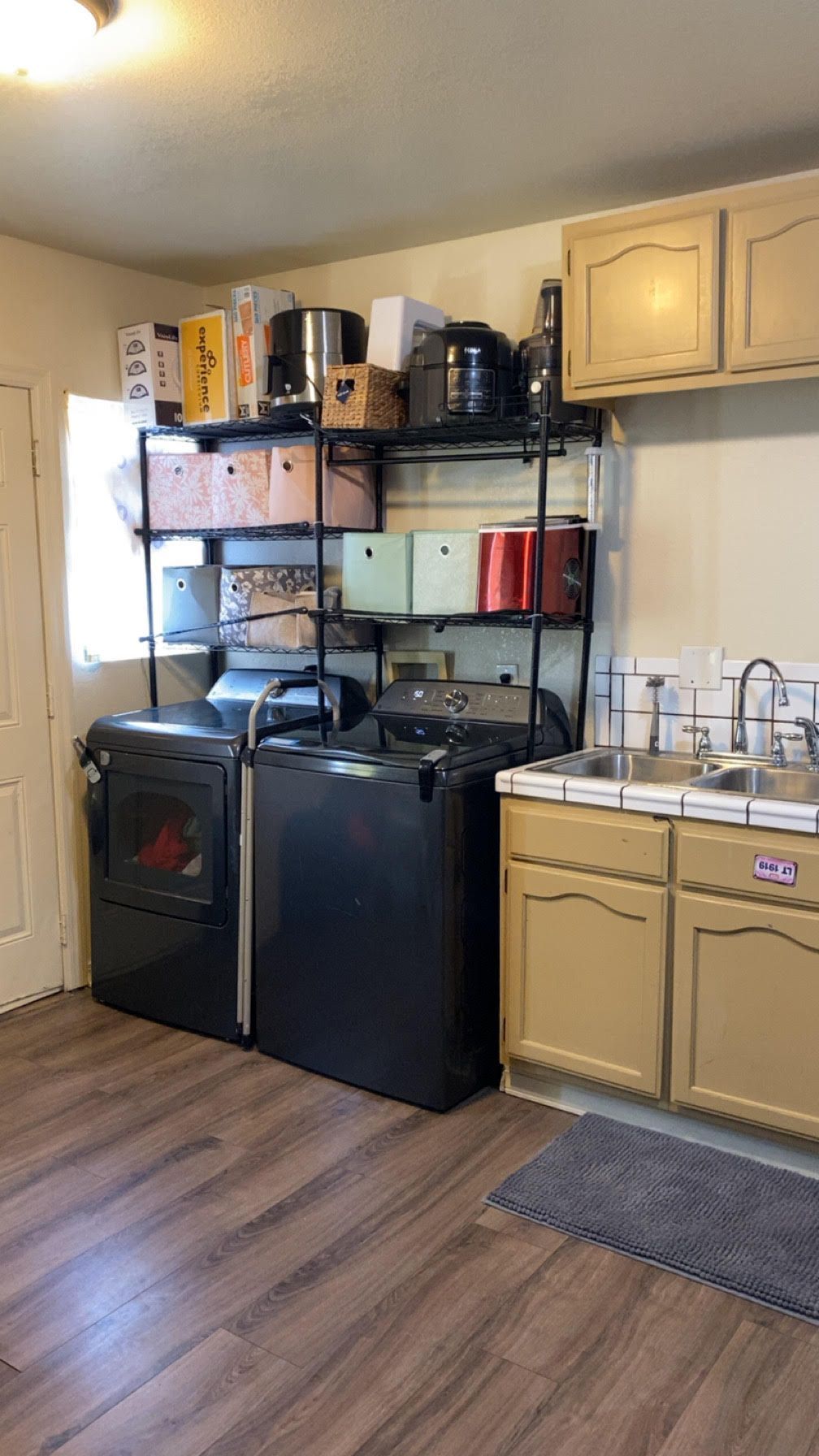 Small kitchen with shelves, cabinets, black refrigerator and stove, and wood-look flooring.