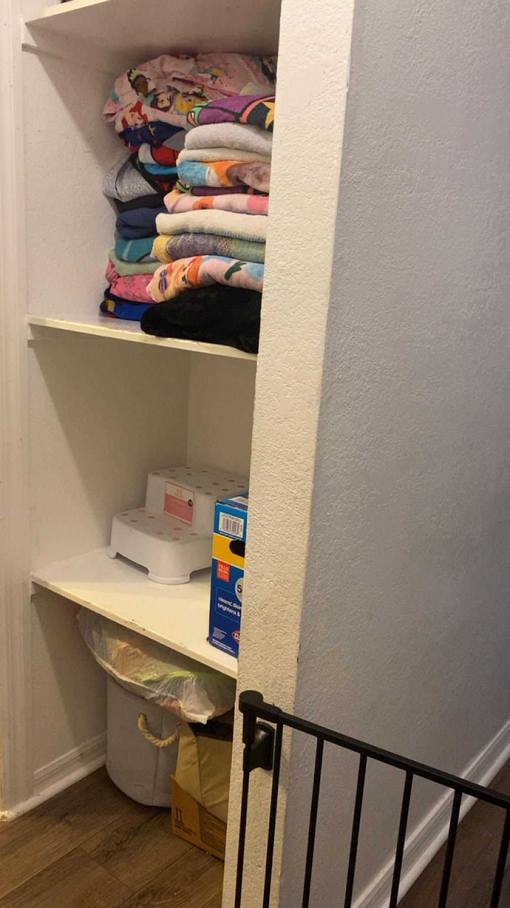 Built-in closet shelves with folded clothes, a small box, and laundry hamper beside a stair railing