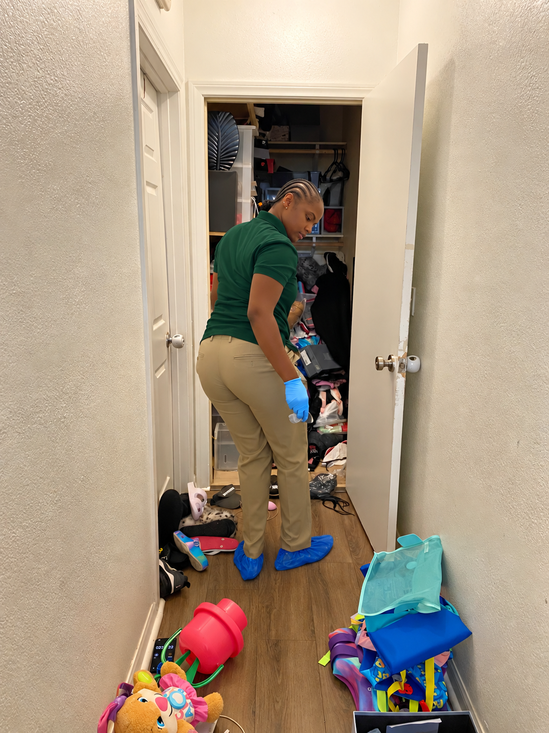 Person organizing toys in a narrow hallway outside a closet, with scattered colorful items on the floor.