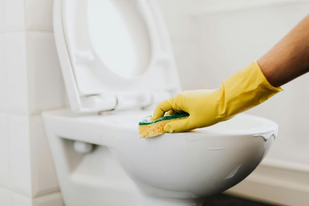 Gloved hand scrubbing a toilet bowl with a sponge in a bathroom