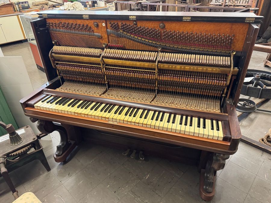 An upright piano with its front cover removed, exposing the internal metal frame, strings, hammers, and yellowed keys.