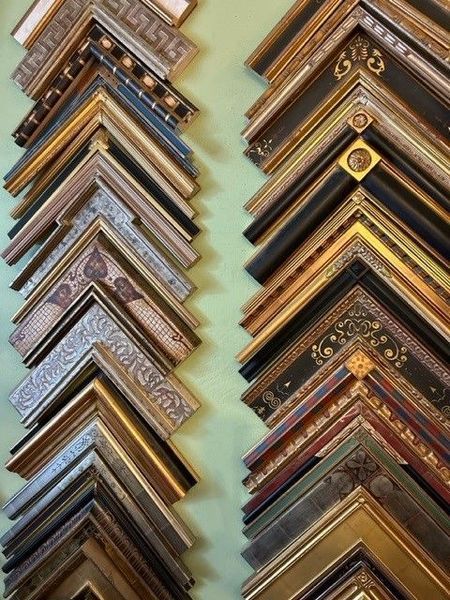 Assorted ornate picture frame samples stacked in two columns, showing gold, wood, and metallic finishes