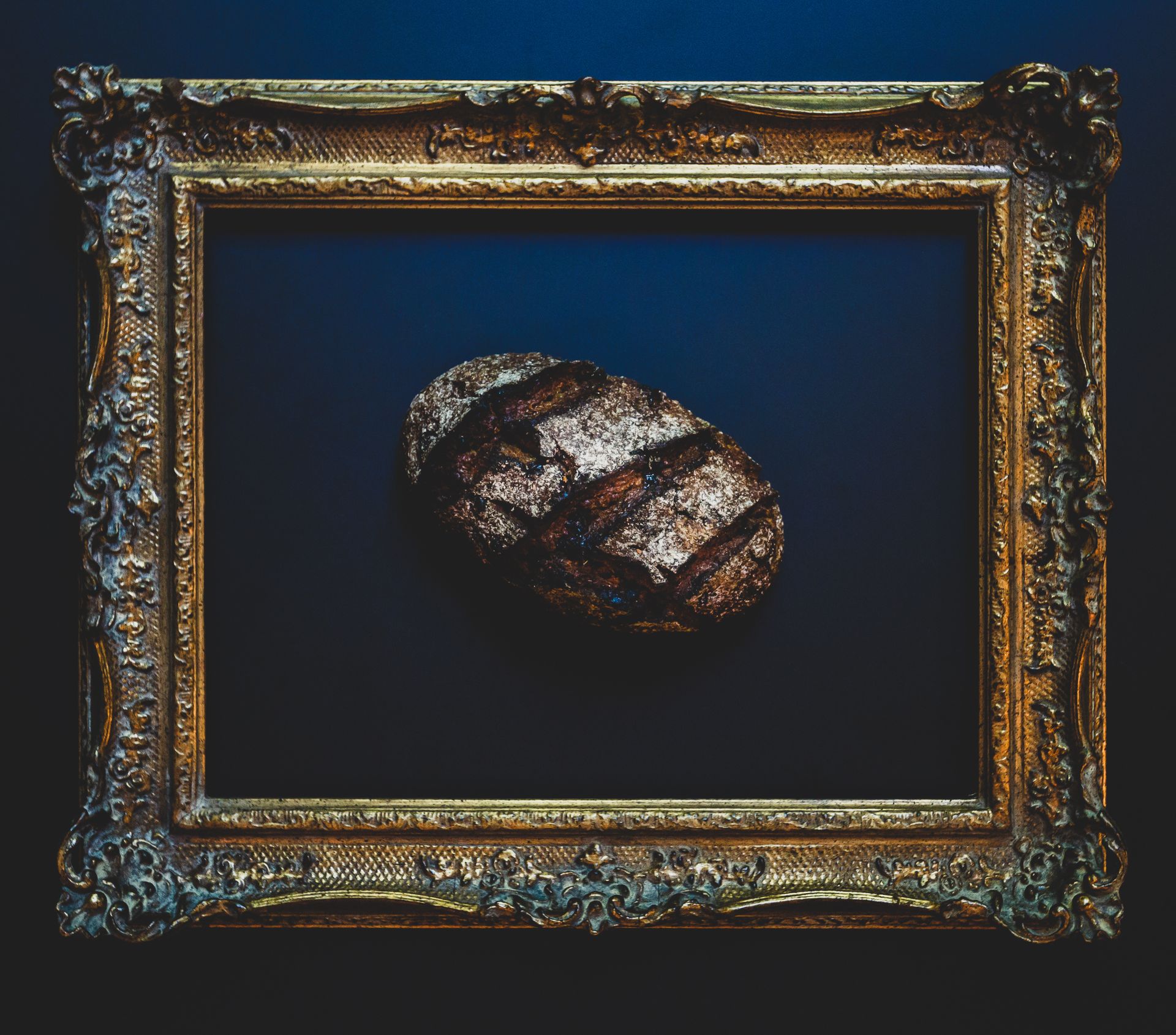 Ornate gold frame around a dark blue background with a small textured oval object in the center Ornate gold frame around a dark blue background with a small textured oval object in the center