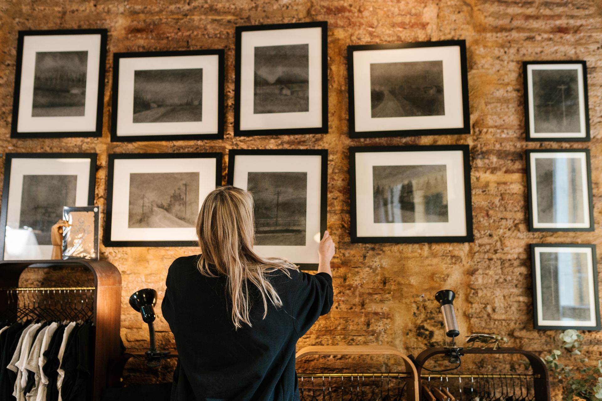 Person hanging framed photos on a brick gallery wall with black-and-white artwork. Person hanging framed photos on a brick gallery wall with black-and-white artwork.