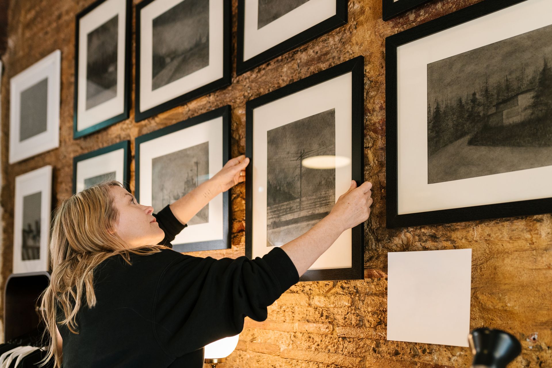 Person hanging framed artwork on a gallery wall of black-and-white photos Person hanging framed artwork on a gallery wall of black-and-white photos