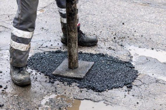 person in work boots and gray pants with reflective stripes using a small stamping post to compact asphalt repairing pothole