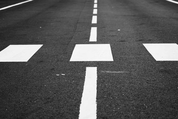 black pavement with white striping. dashed white line down the middle with white crosswalk in foreground.