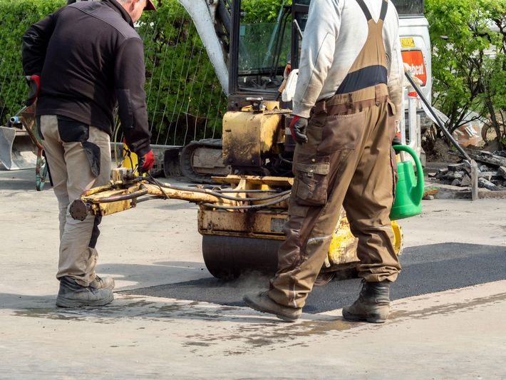 two men working a waist-high yellow machine to compact asphalt -repairing parking lot