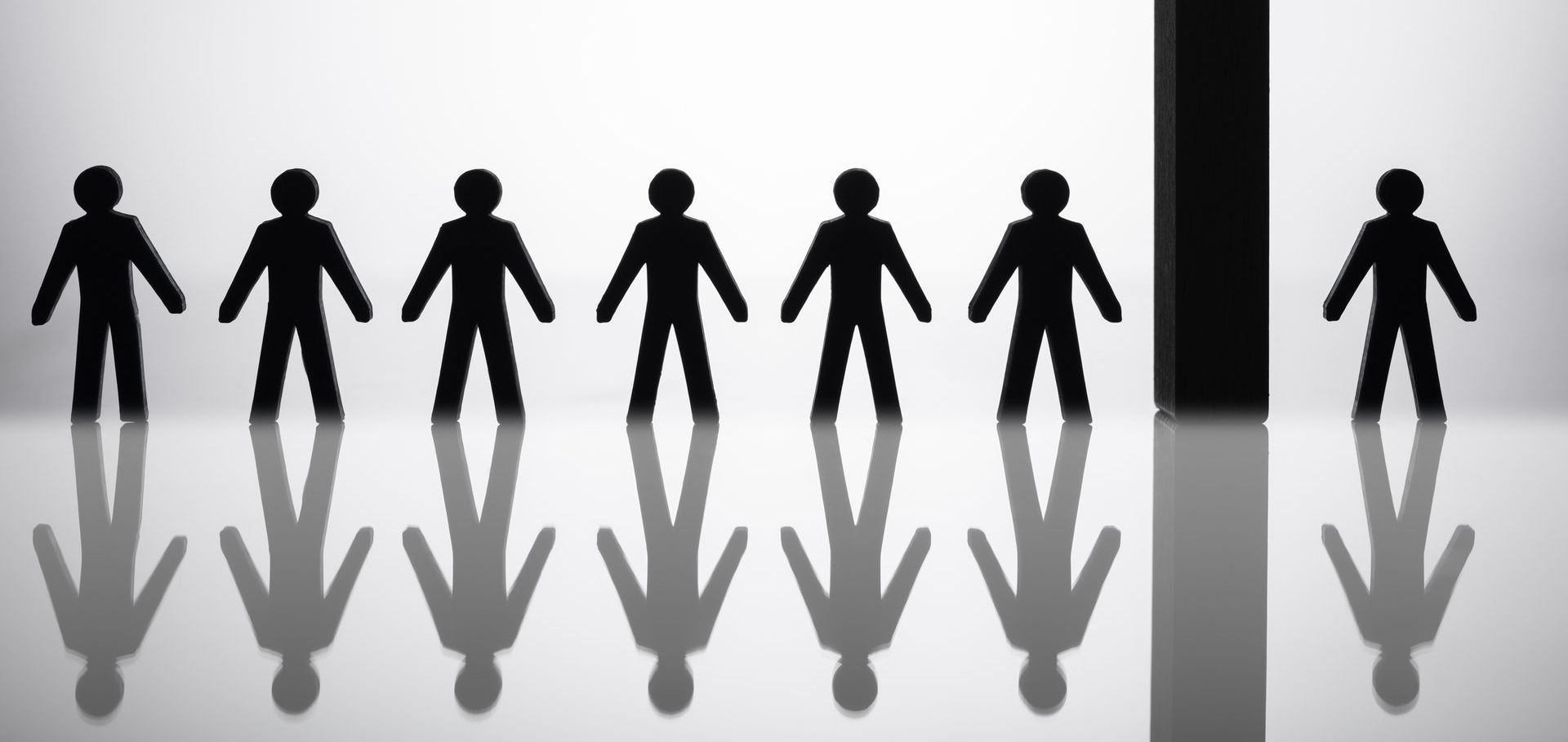 Paper cutout figures with one separated by a barrier, symbolizing social exclusion and discrimination.