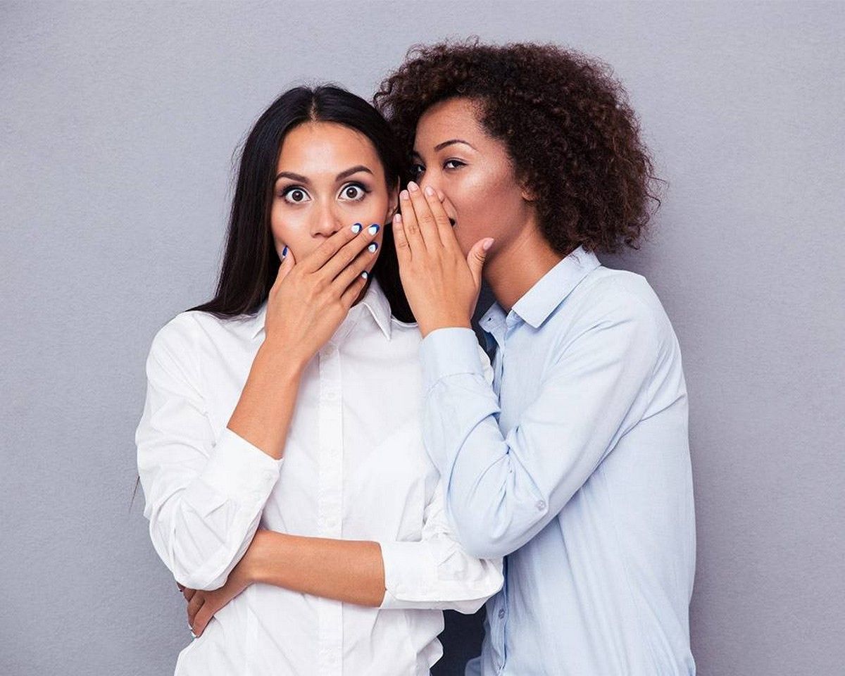 Two women sharing a secret, symbolizing the challenge of judgmental people.
