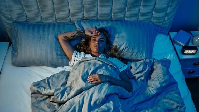 An exhausted woman lying awake in bed at night, illustrating the cycle of pregnancy sleep problems a