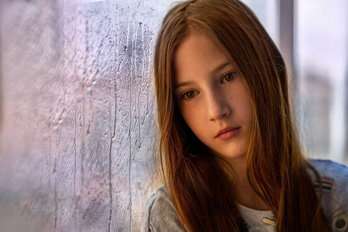 Teen girl looking out a rainy window, representing youth loneliness and mental health support in Albuquerque.