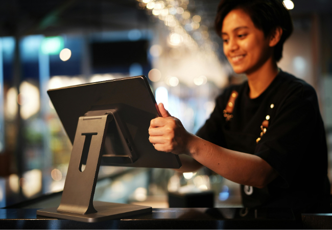 Eine lächelnde Person bedient ein Touchscreen-Kassensystem in einem Geschäft.