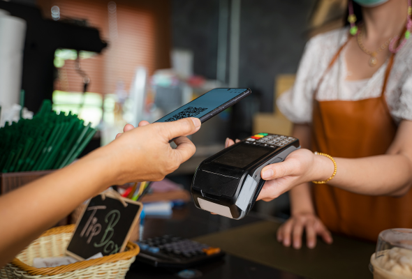 Bezahlen mit dem Handy in der Nähe eines Zahlungsterminals an der Theke eines Cafés.