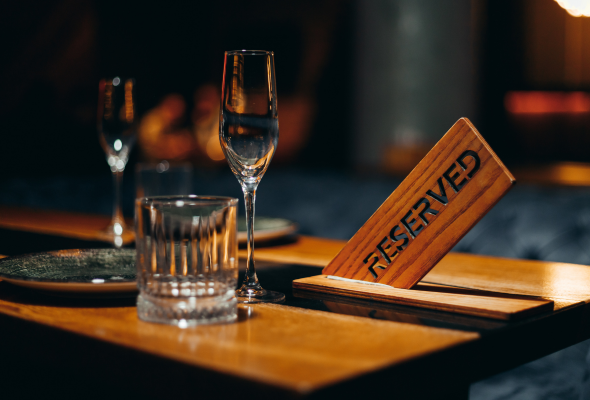Ein hölzernes Schild mit der Aufschrift „Reserviert“ steht auf einem Tisch neben Gläsern in einem Restaurant.