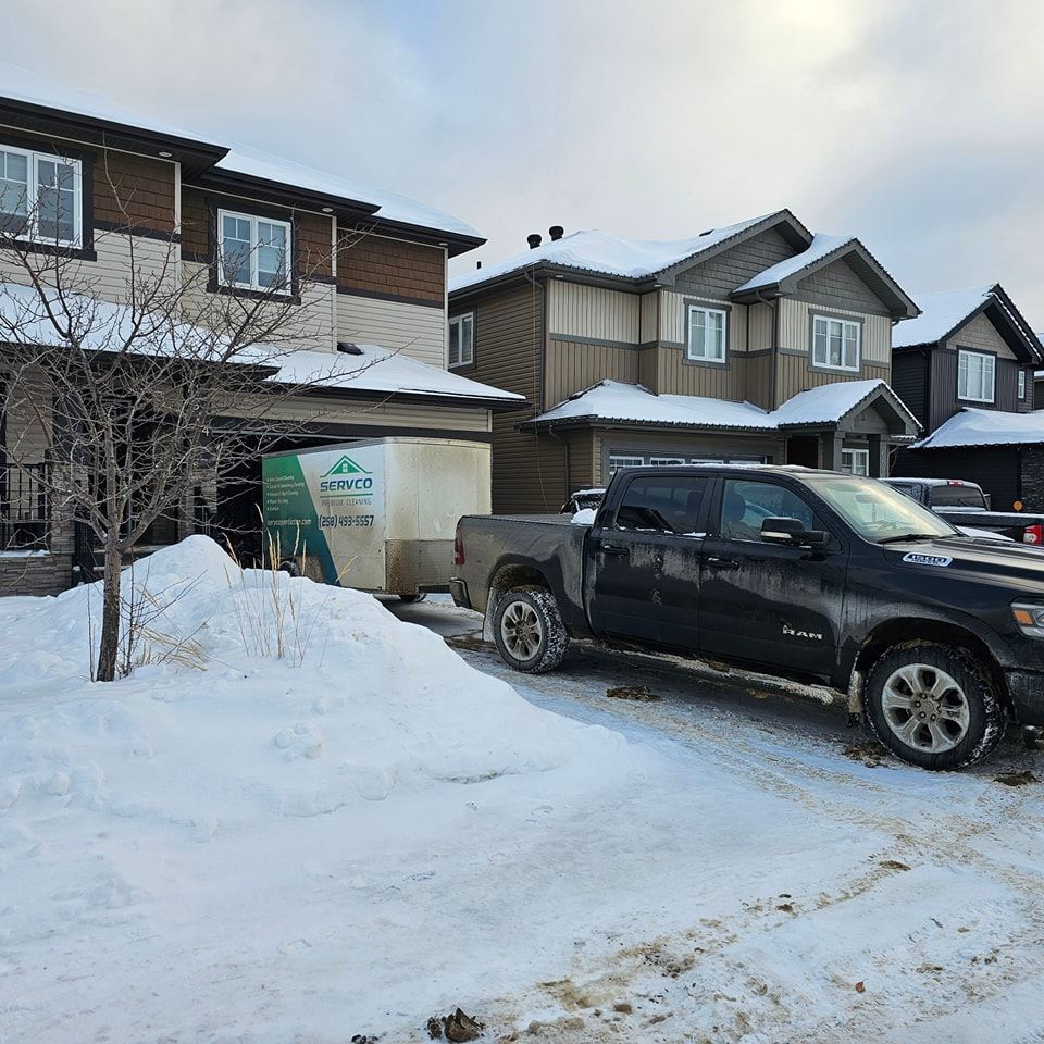 A truck is parked in the snow in front of a house