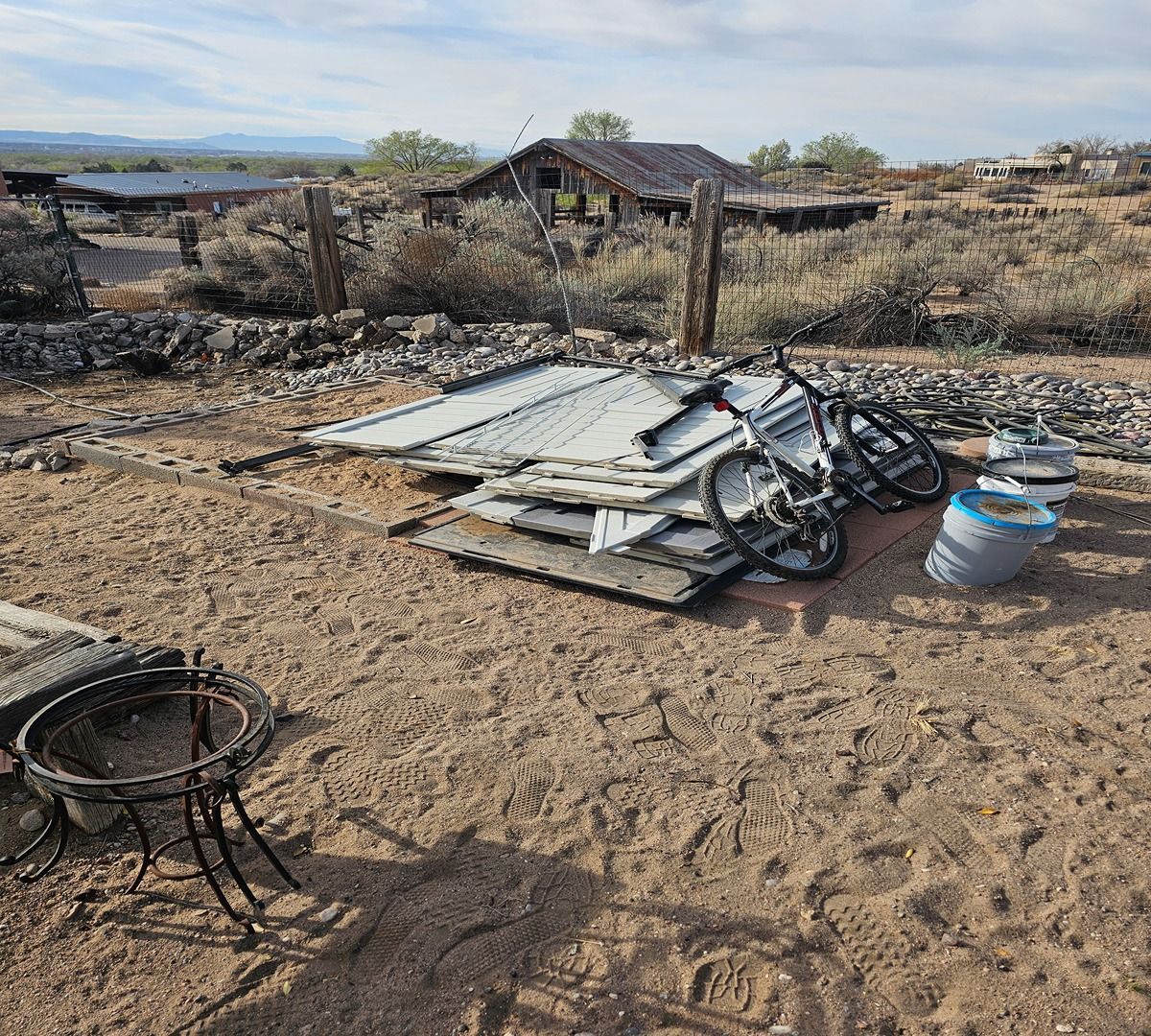 Burned-out yard with scattered debris, a bicycle, and a charred structure in a dry rural landscape