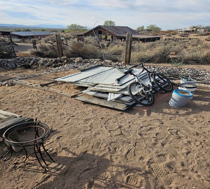 Burned-out yard with debris, collapsed metal sheet, and a bicycle in a dry, damaged landscape