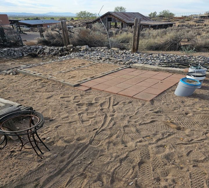 Sandy backyard with stone patio pavers, a fire pit, and a small shed in the distance.