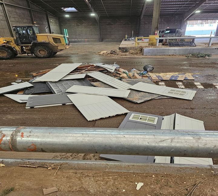 Warehouse floor with scattered metal roofing panels, debris, and a yellow loader in the background