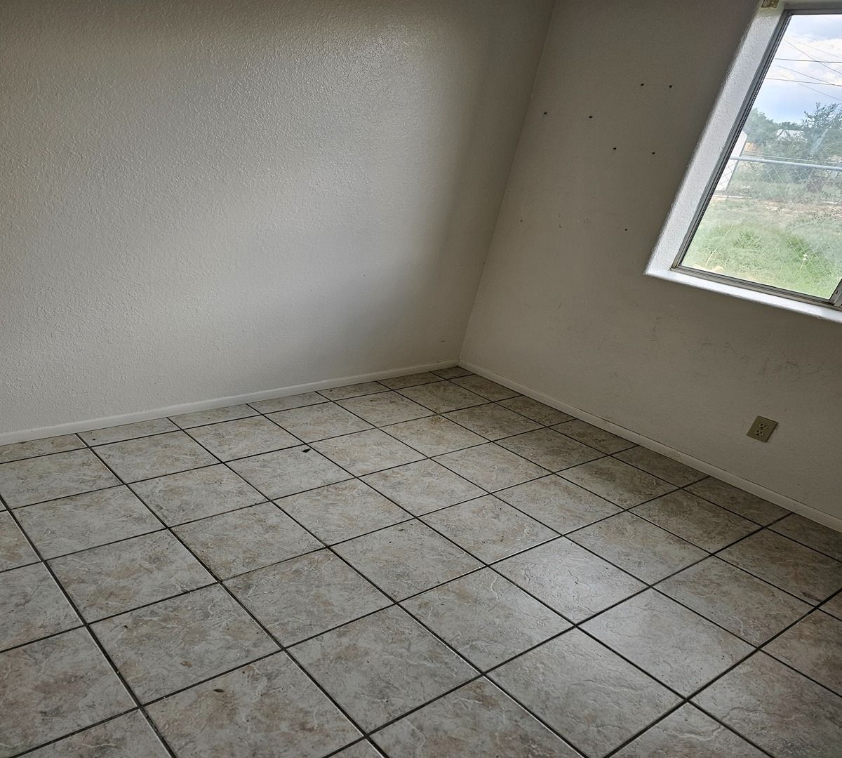 Empty tiled room with white walls and a window letting in daylight