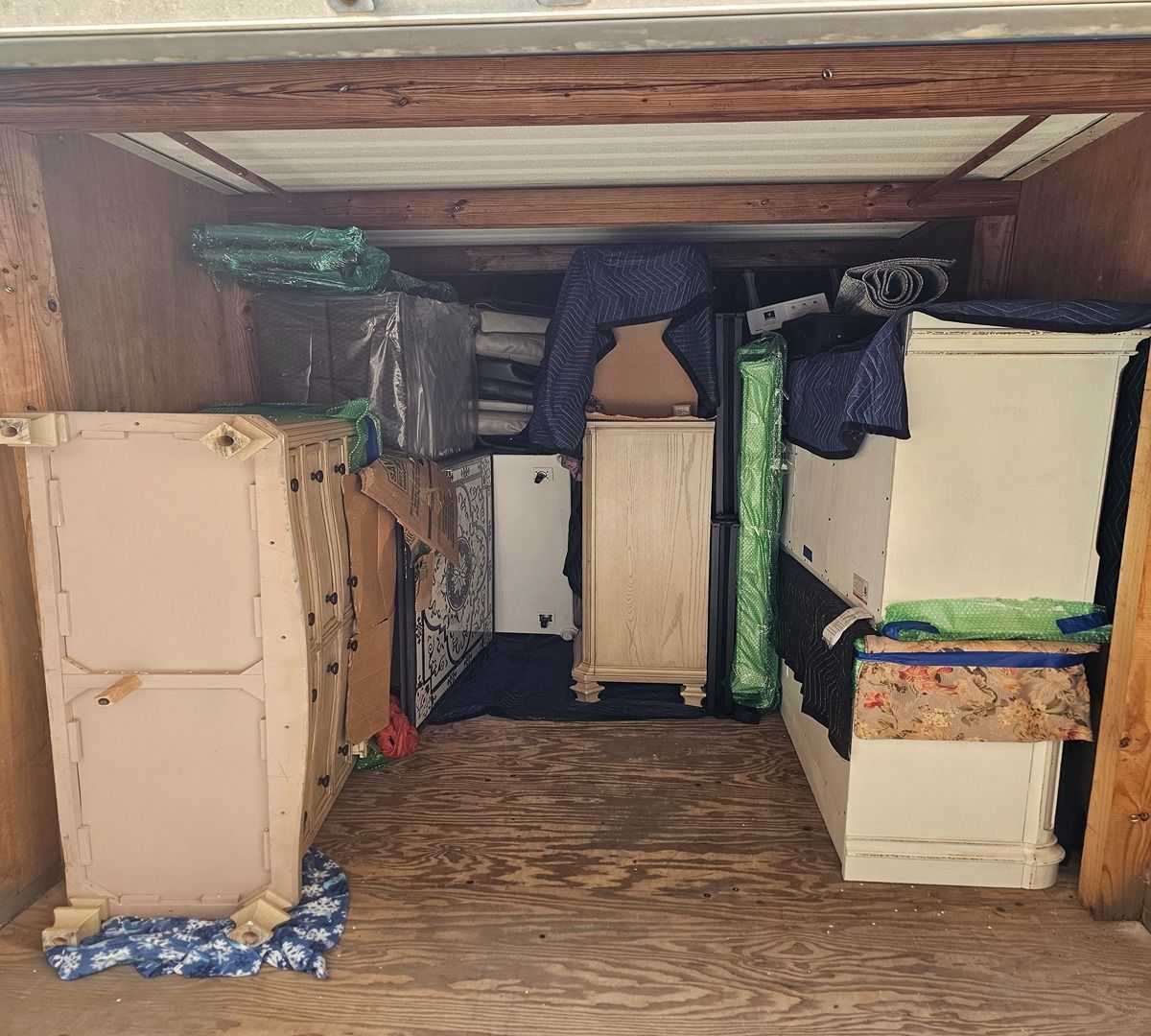 Wooden crawlspace with stacked boxes, wrapped pipes, and storage items under a floor opening