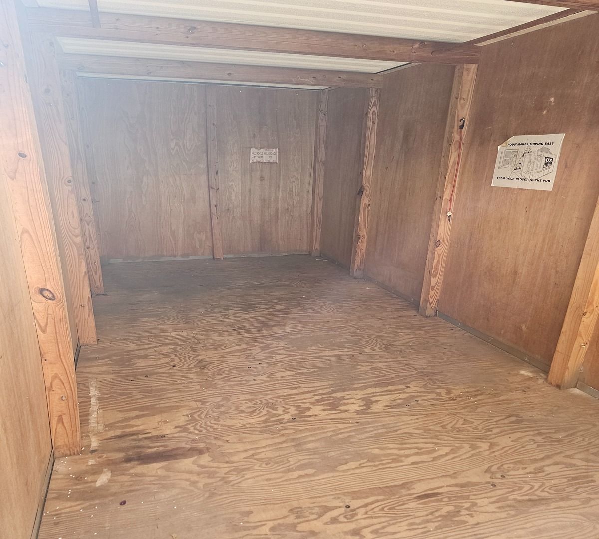 Empty wooden storage shed with plywood floor and walls, viewed from the entrance.