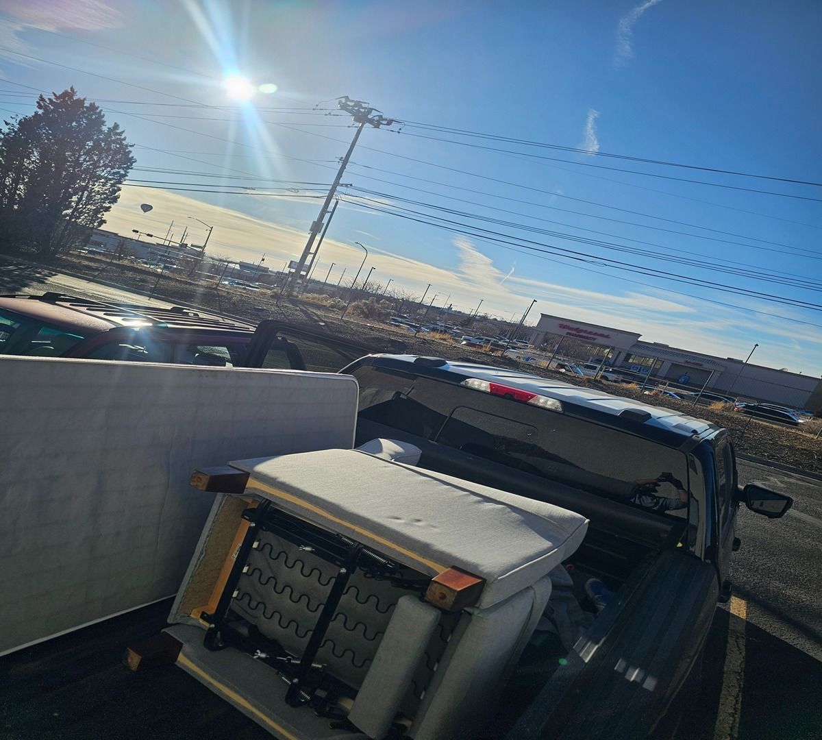 Sunlit parking lot view with a truck bed, white trailer, power lines, and city skyline in the distance
