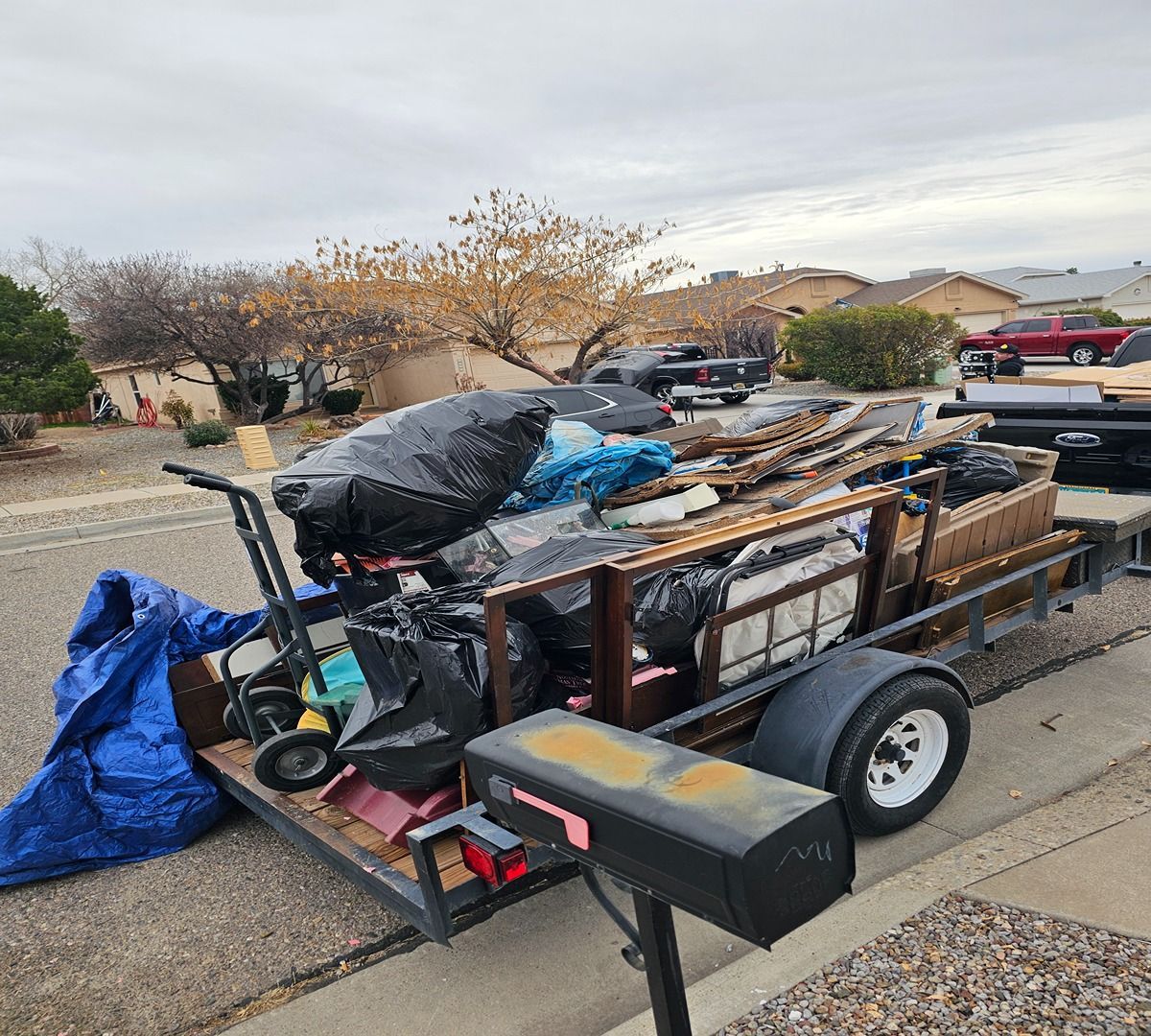 Loaded utility trailer piled with yard debris and tools in a suburban driveway