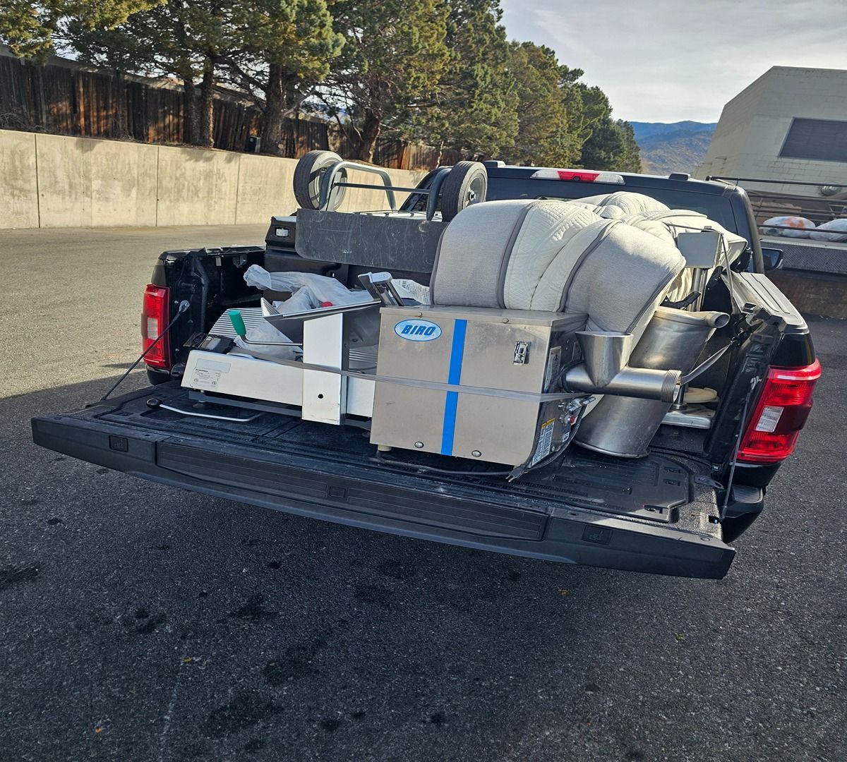 Pickup truck loaded with furniture and boxes in a parking lot, with blankets and metal parts in the open bed