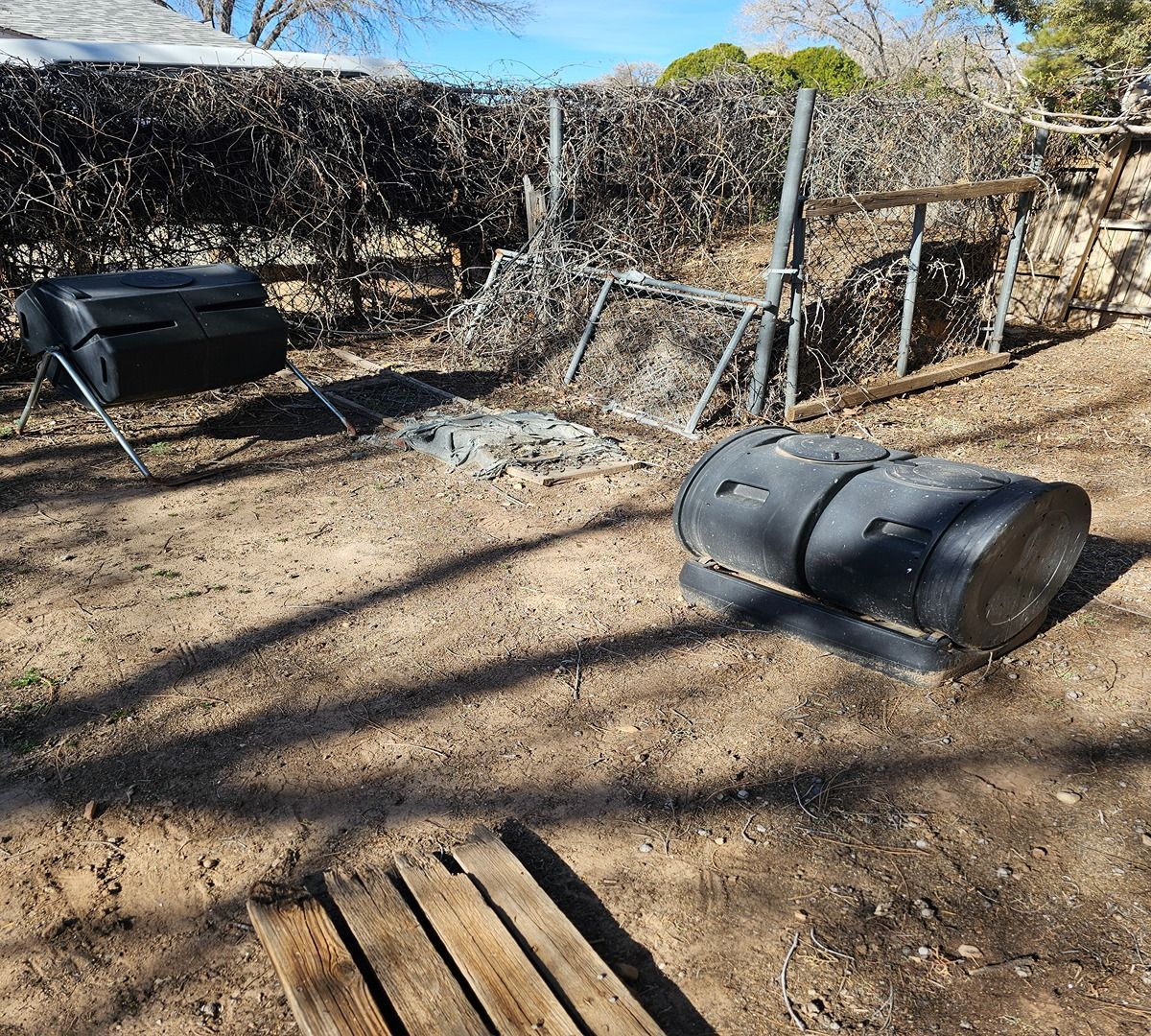Backyard with two black metal fire pits, a wire fence, dry ground, and trees in the background