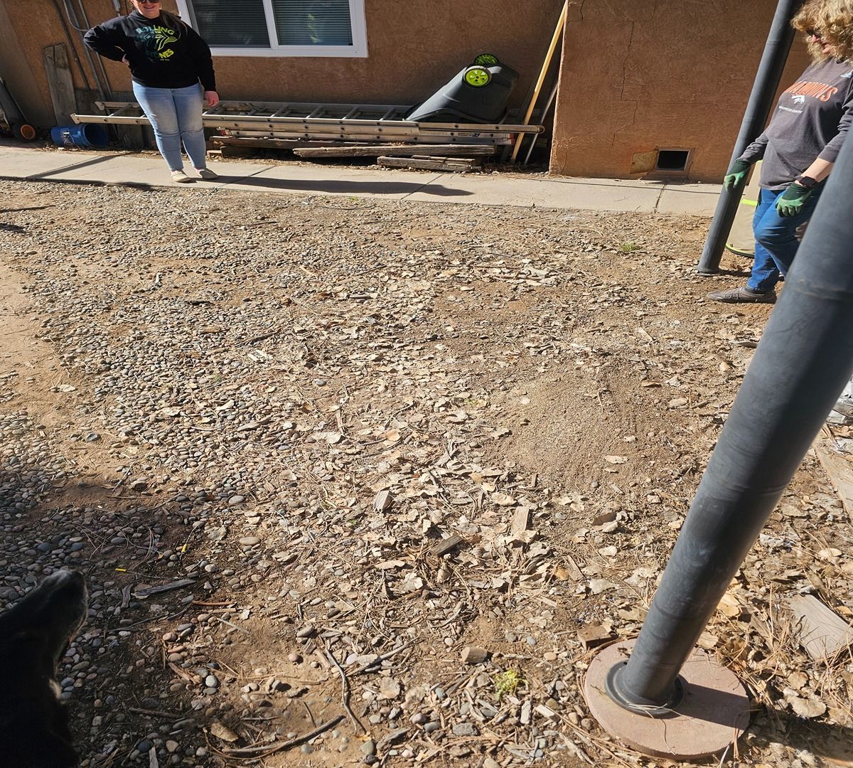 Workers leveling gravel in a backyard beside a house and patio steps