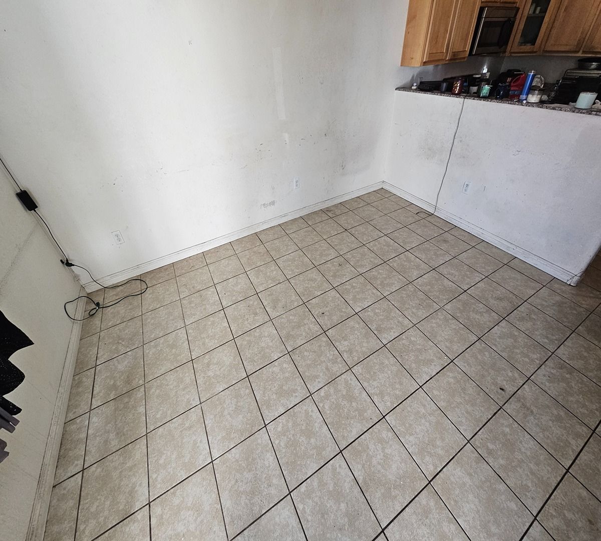 Empty tiled corner of a small room with white walls, wood cabinets, and a countertop.
