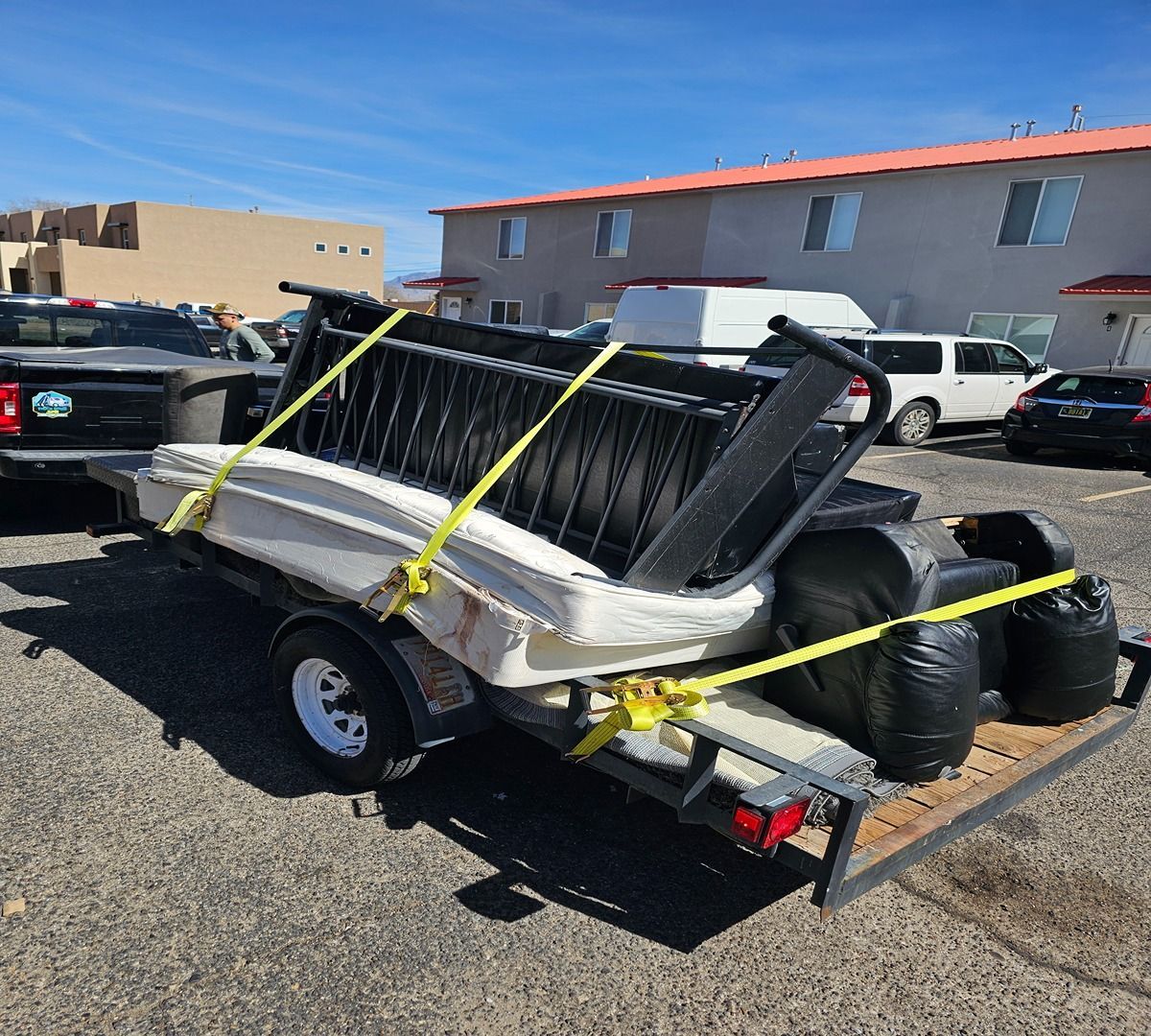 Damaged white boat strapped on a trailer in a parking lot under a clear blue sky