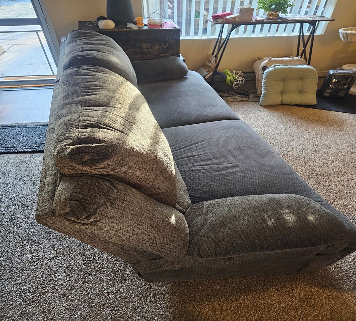 Dark gray sectional sofa in a sunlit living room with carpet and windows.