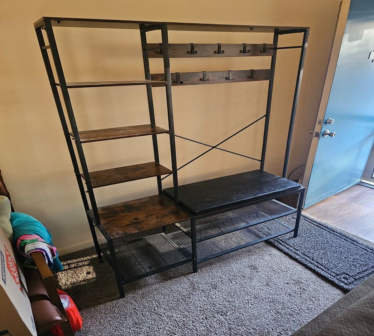 Black metal shelving unit and bench in a carpeted entryway near a doorway.