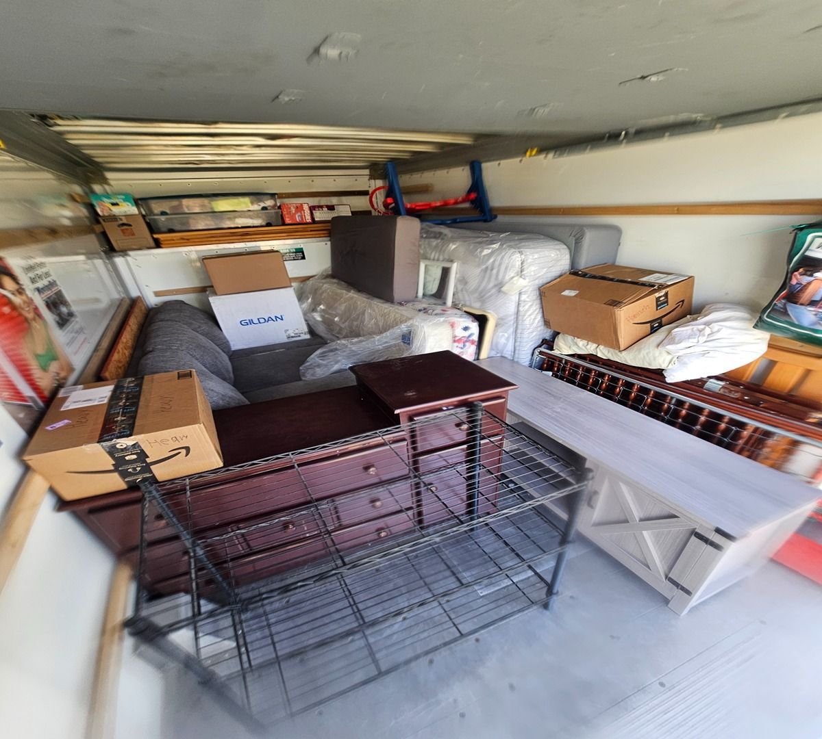 Cluttered storage room with stacked boxes, wire crates, and plastic bins under a low ceiling.