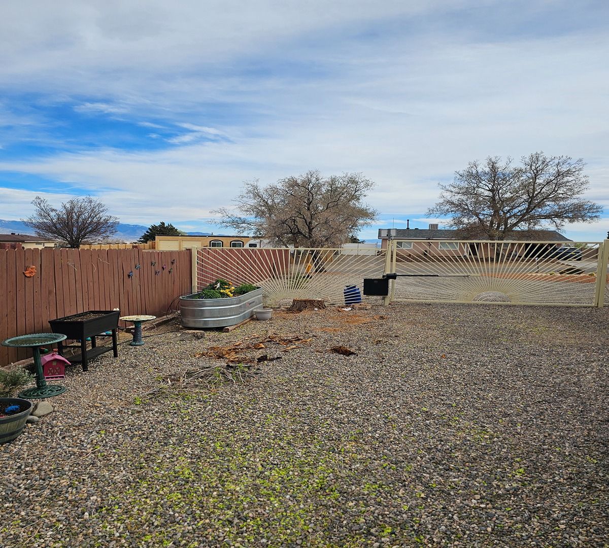 Open backyard with gravel, wooden fence, raised garden beds, and leafless trees under a cloudy sky