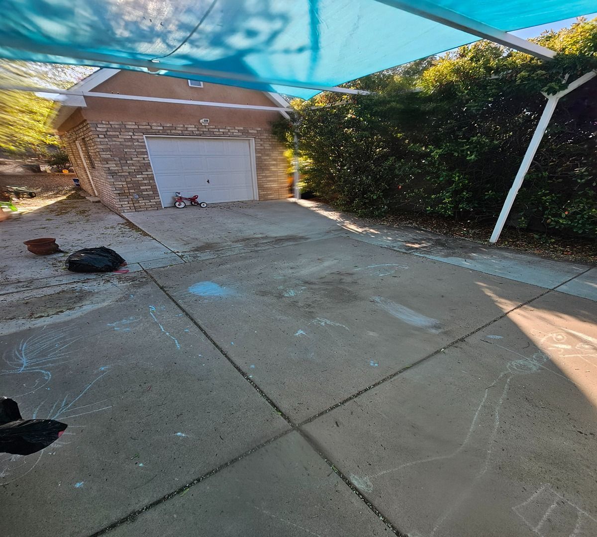 Concrete driveway under blue shade sails leading to a closed garage door beside a hedge