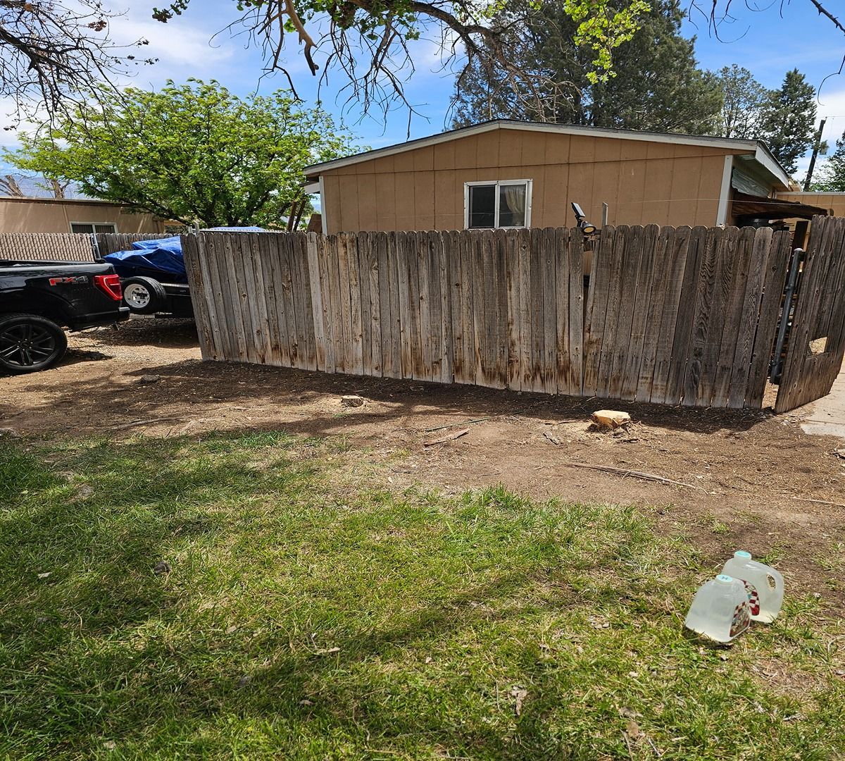 Weathered wooden fence in front of a beige house, with a parked ATV and grassy yard under a blue sky.